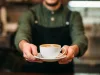 Waiter in black apron stretches a cup of coffee