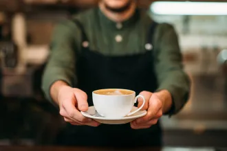Waiter in black apron stretches a cup of coffee
