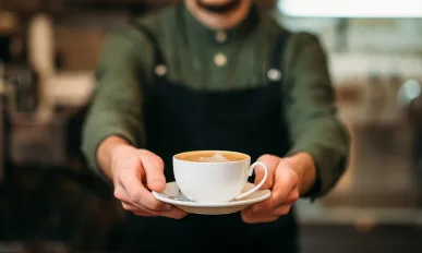Waiter in black apron stretches a cup of coffee