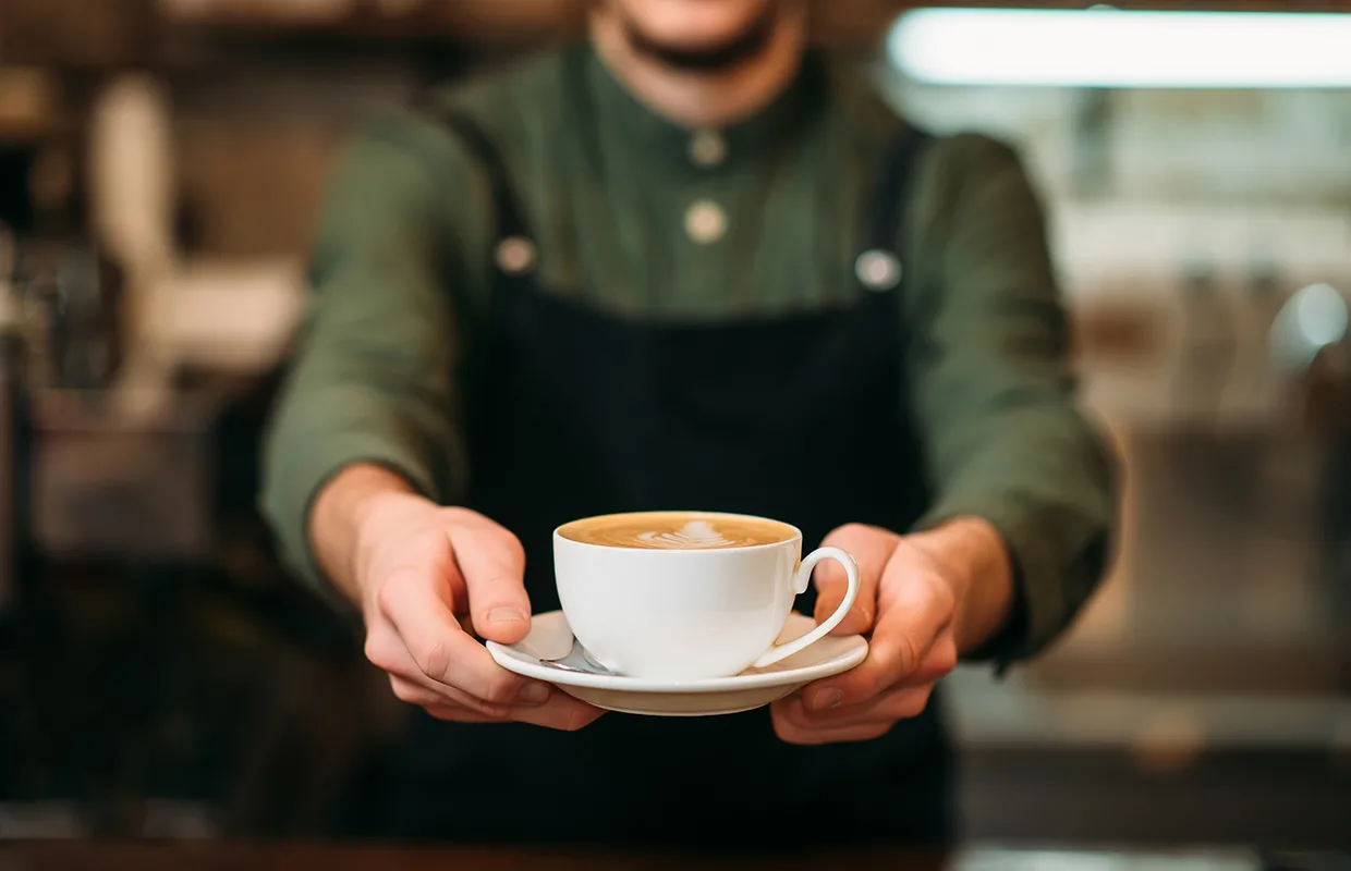 Waiter in black apron stretches a cup of coffee