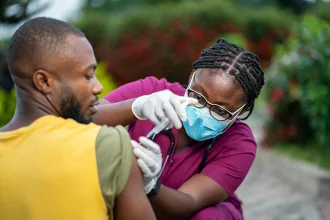 image of young african nurse in face mask, injecting young black