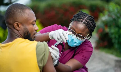 image of young african nurse in face mask, injecting young black